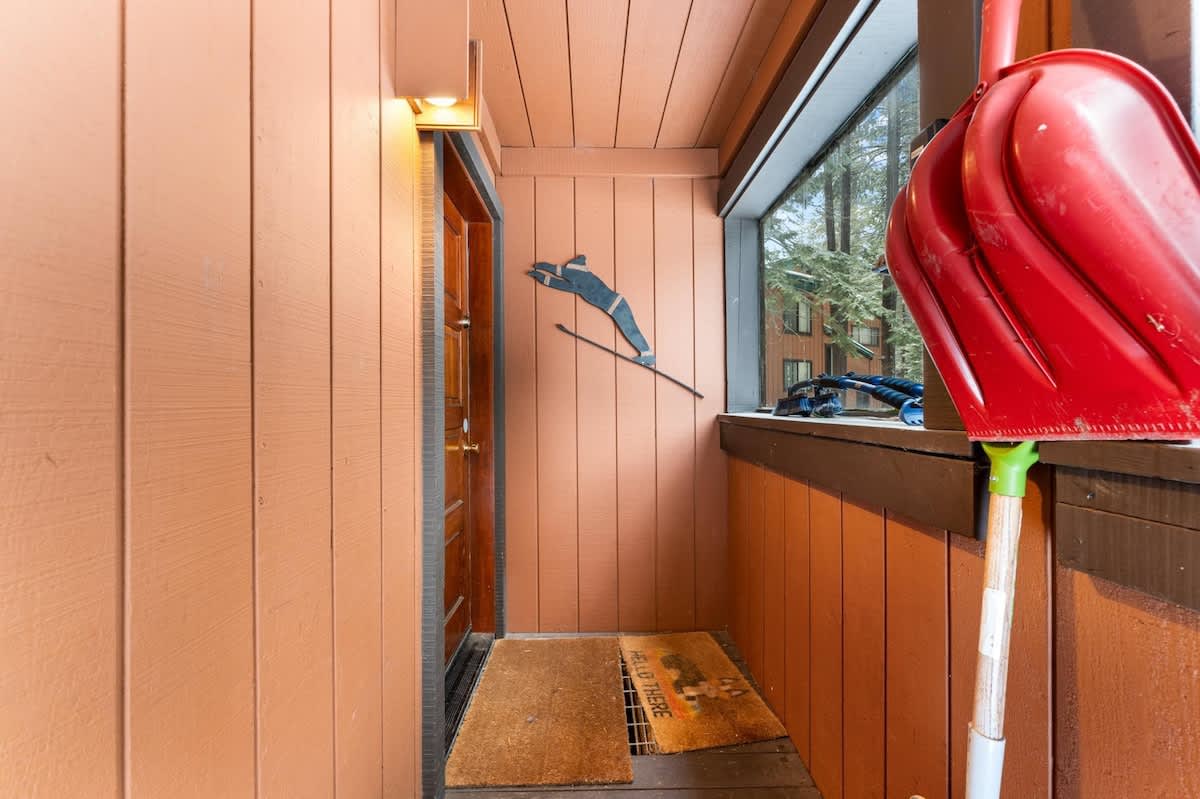 Wooden entryway of a Truckee vacation rental with a welcome mat, red snow shovel, and skier wall decoration.