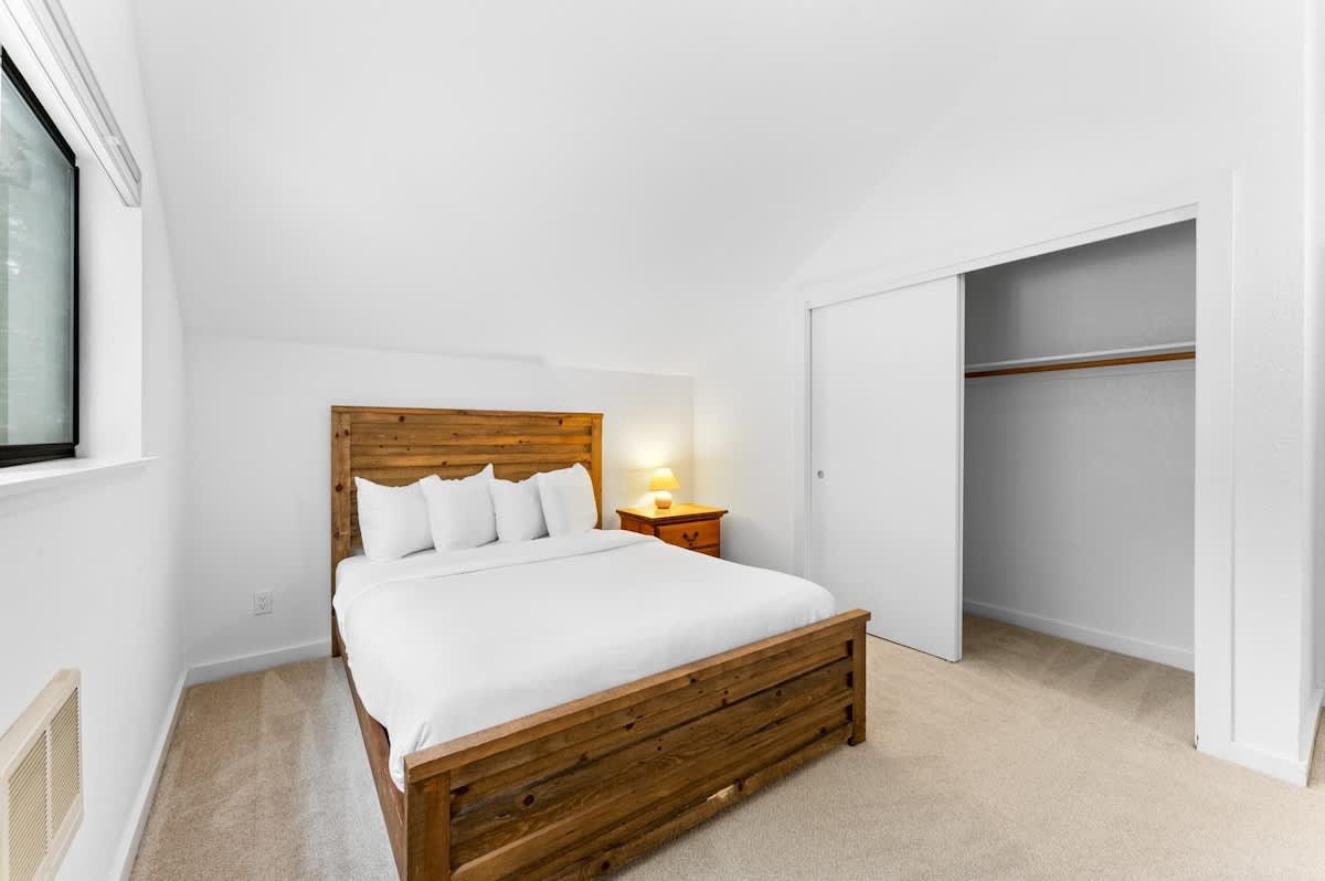 Cozy bedroom in a Truckee vacation rental with a wooden bed frame, white linens, bedside lamp, and open closet.