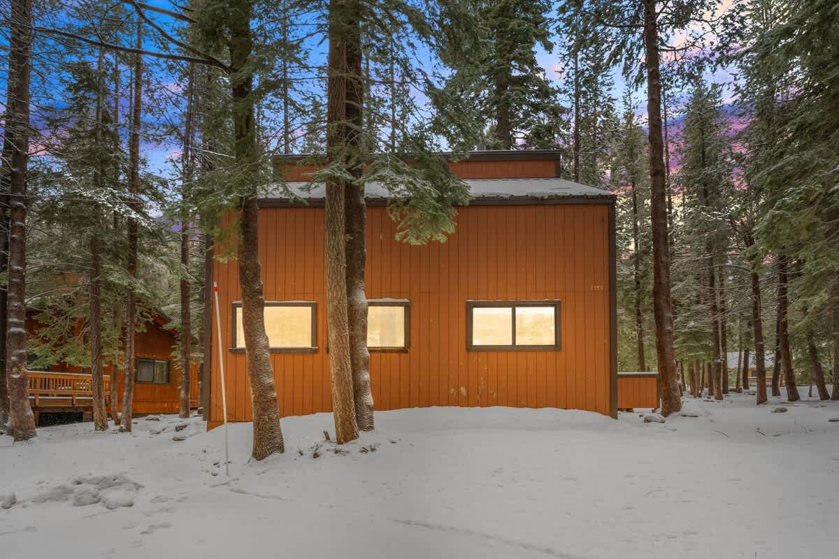 Wooden cabin in snowy forest, Truckee vacation rental at twilight, surrounded by tall trees.