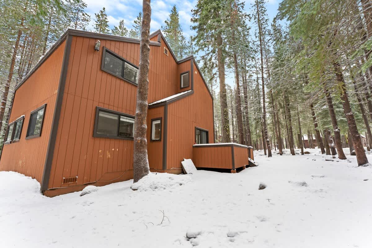 A cozy, snow-covered vacation rental cabin surrounded by tall trees in Truckee.