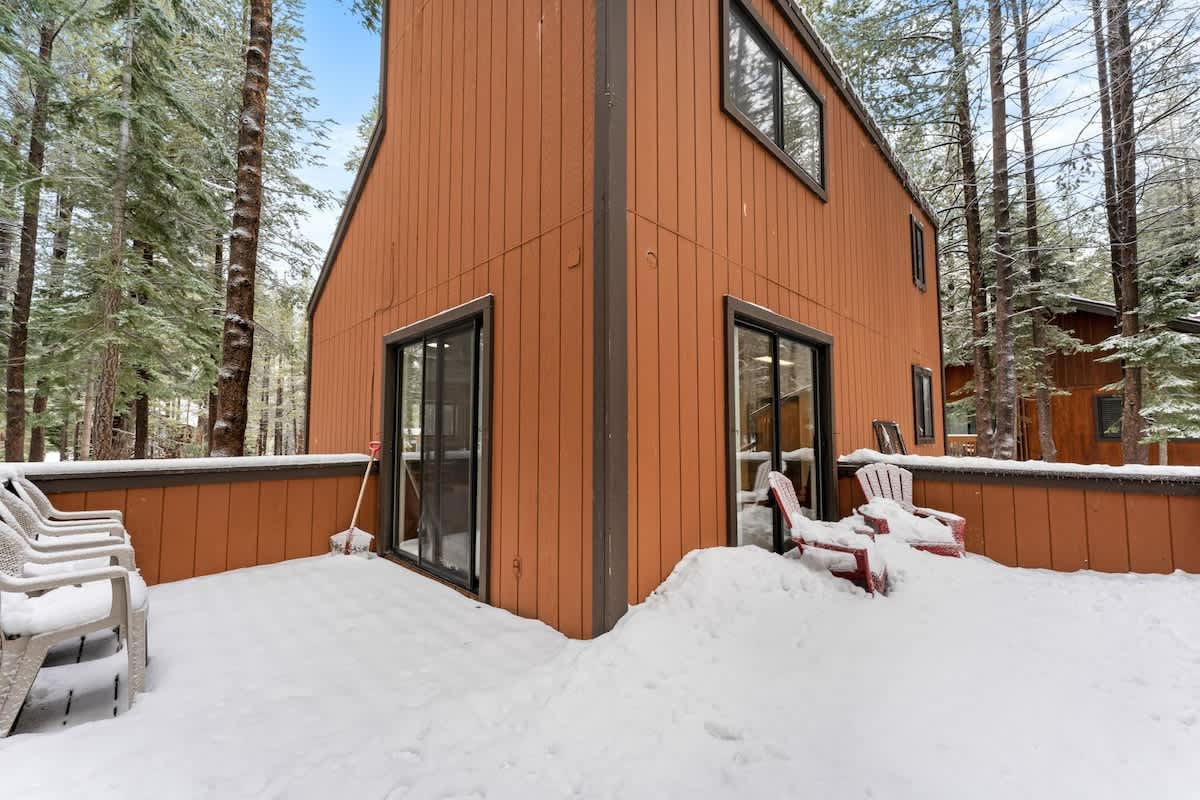 A snowy cabin in Truckee surrounded by trees, featuring a cozy vacation rental with red chairs and sliding glass doors.