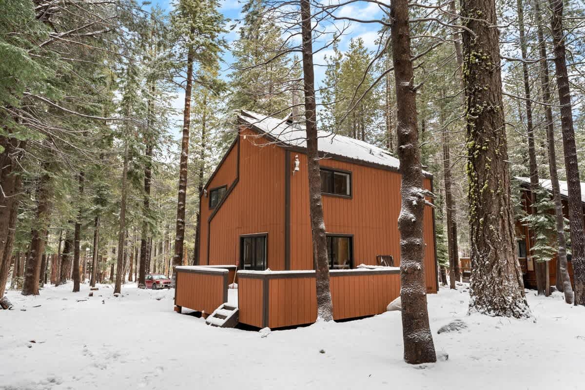 A cozy vacation rental in snowy woods of Truckee, featuring a brown cabin surrounded by tall trees in winter.