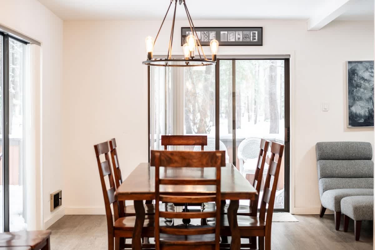 Cozy dining area in a Truckee vacation rental with wooden table and chairs, bright natural light through glass doors.