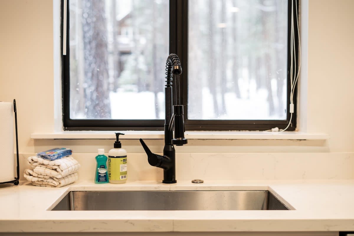 Modern kitchen sink with soap and towels in a Truckee vacation rental, featuring a snowy forest view through the window.