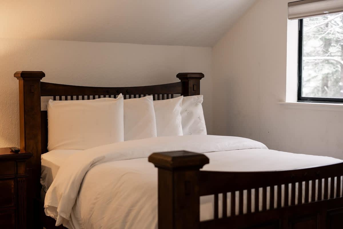 Cozy bedroom in a Truckee vacation rental with a wooden bed frame, white bedding, and a window with a snowy view.