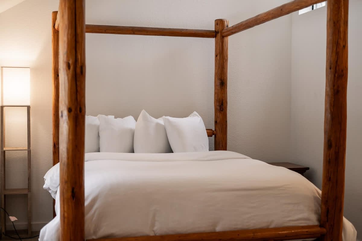 Cozy bedroom with a wooden canopy bed in a Truckee vacation rental, featuring white bedding and soft lighting.