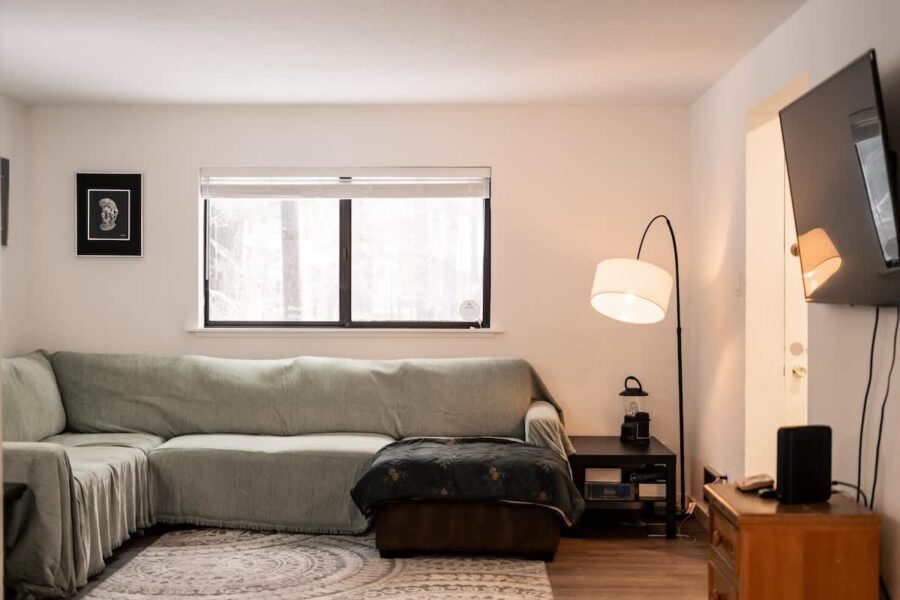 Cozy living room in a Truckee vacation rental with a green sectional sofa, lamp, and window view on a snowy day.