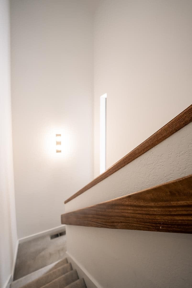 Minimalist staircase with wooden railing in a Truckee vacation rental, softly lit by wall light.