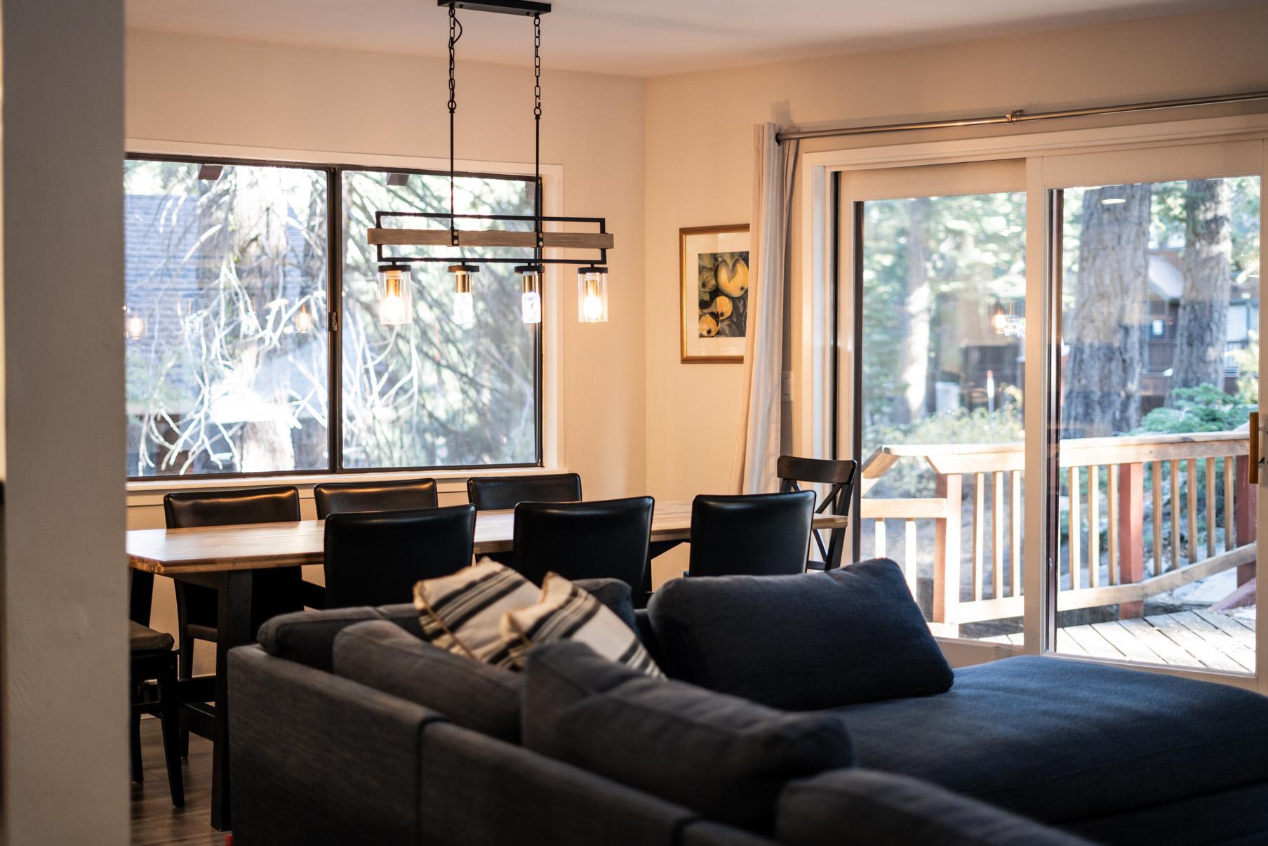 Modern Tahoe Vista vacation rental with a cozy living area, dining table, and large windows overlooking a wooded deck.