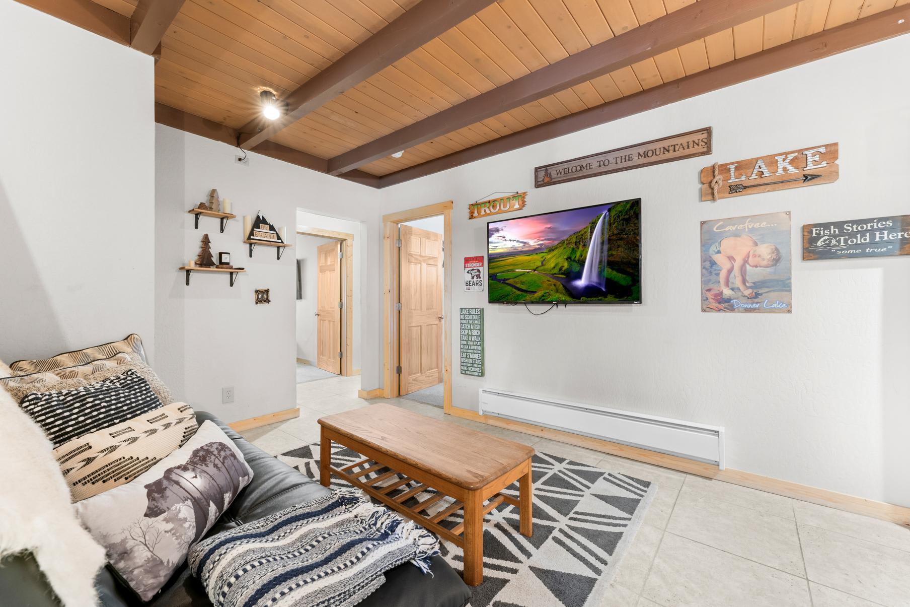 Cozy living room in a Truckee vacation rental with a sofa, wooden table, decorative signs, and a mounted TV.