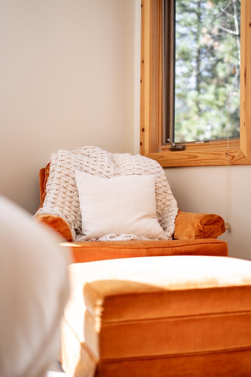 Cozy orange chair with a blanket and pillow in a Truckee vacation rental, next to a wooden-framed window.