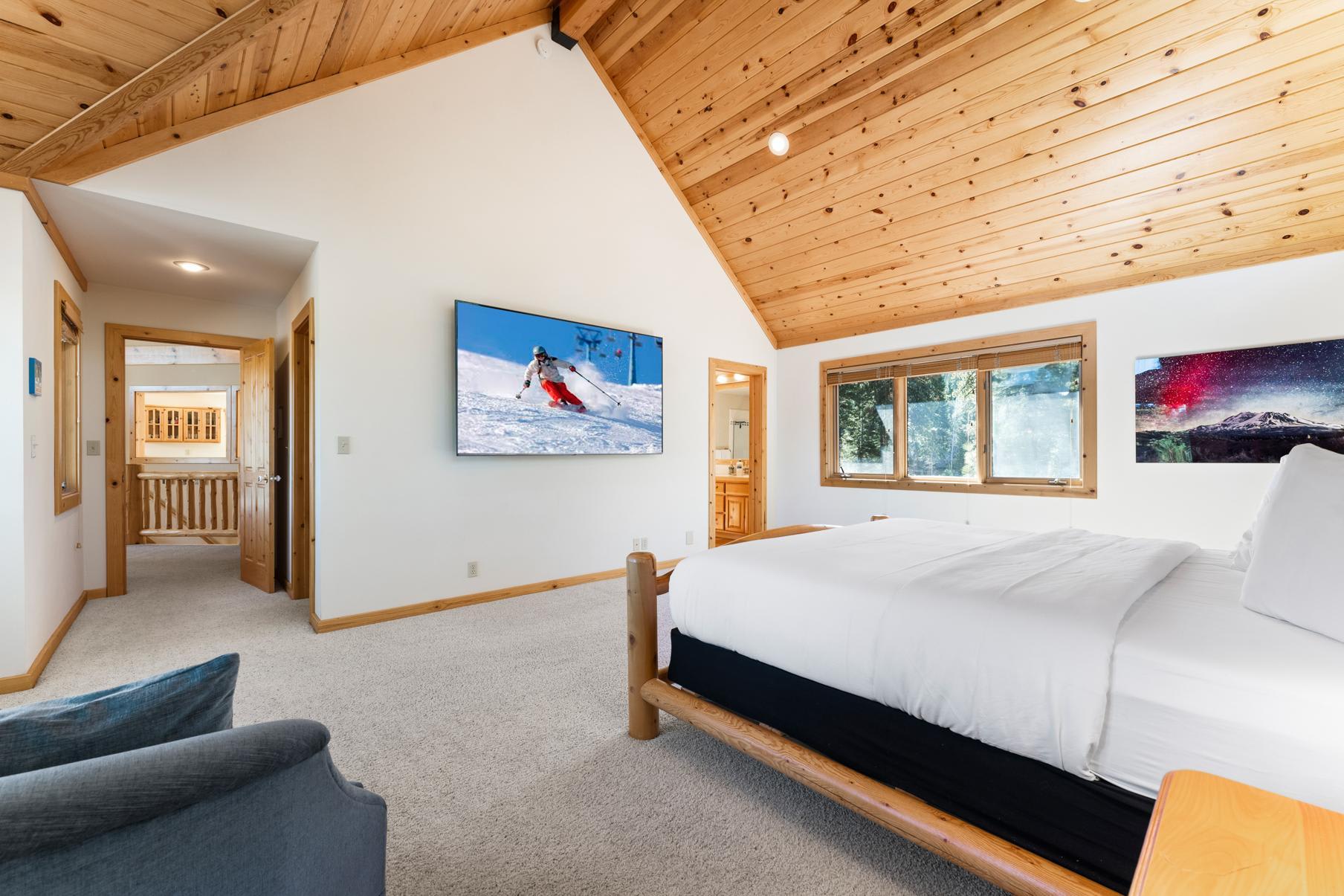 Cozy bedroom in a Truckee vacation rental with wooden ceiling, large bed, and scenic art on the walls.