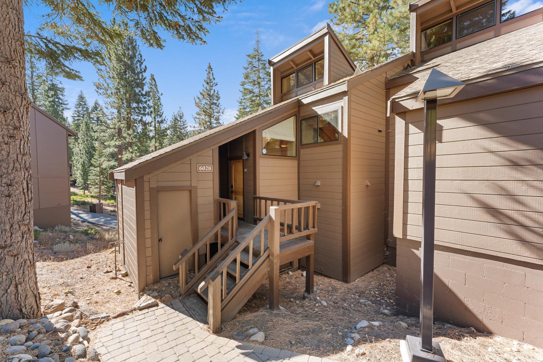 Brown cabin-style vacation rental in Truckee, surrounded by tall pine trees under a clear blue sky.