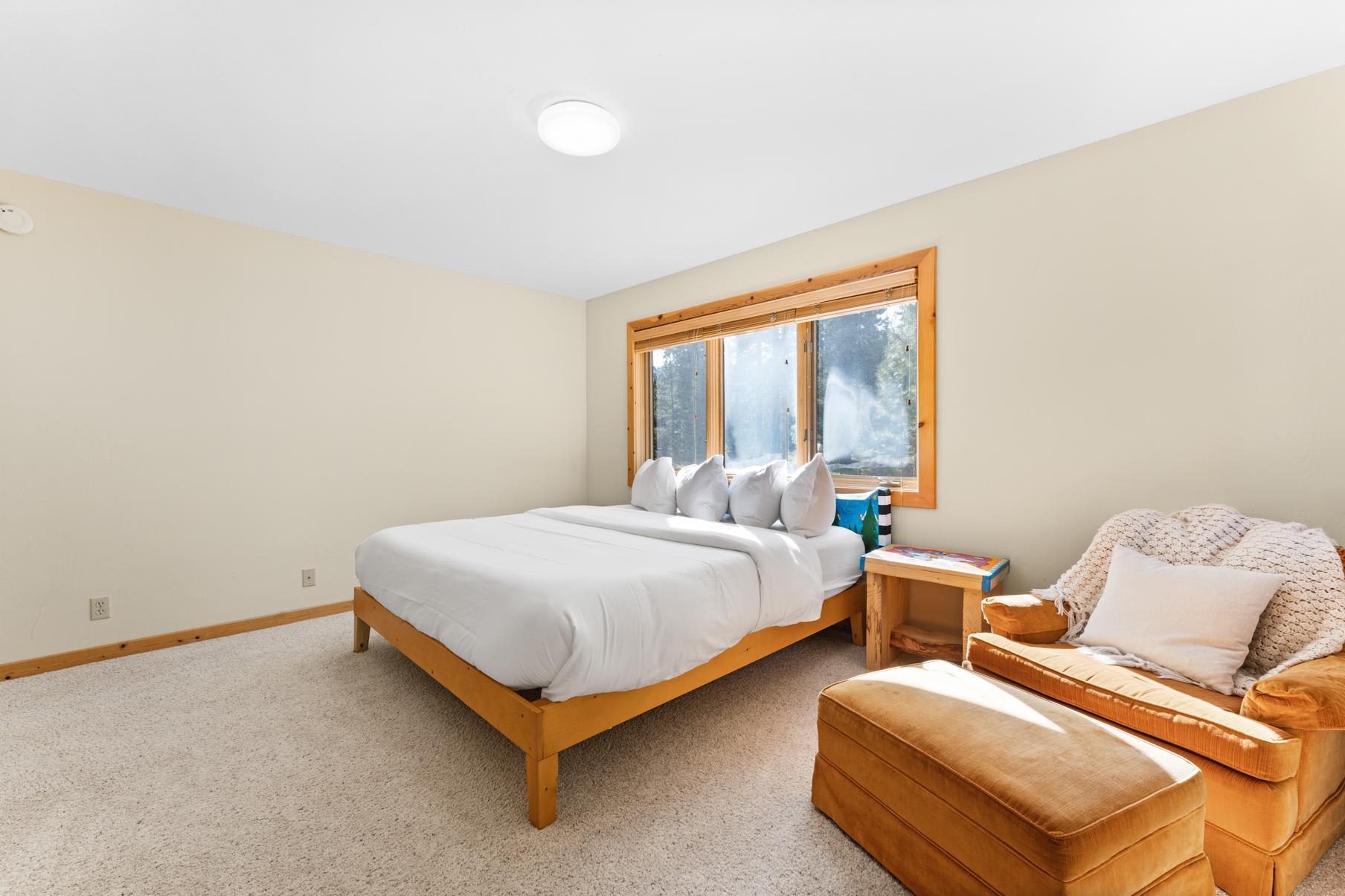 Cozy bedroom in a Truckee vacation rental with a comfy bed, sunlit window, and plush armchair with ottoman.