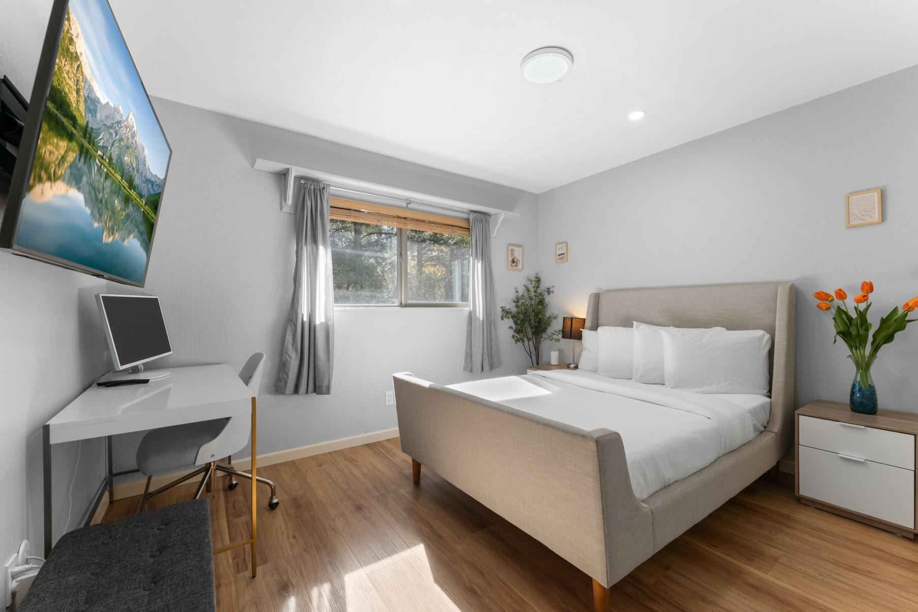 Bright bedroom in a Truckee vacation rental, with modern decor, a cozy bed, a desk, and a view of a sunlit window.