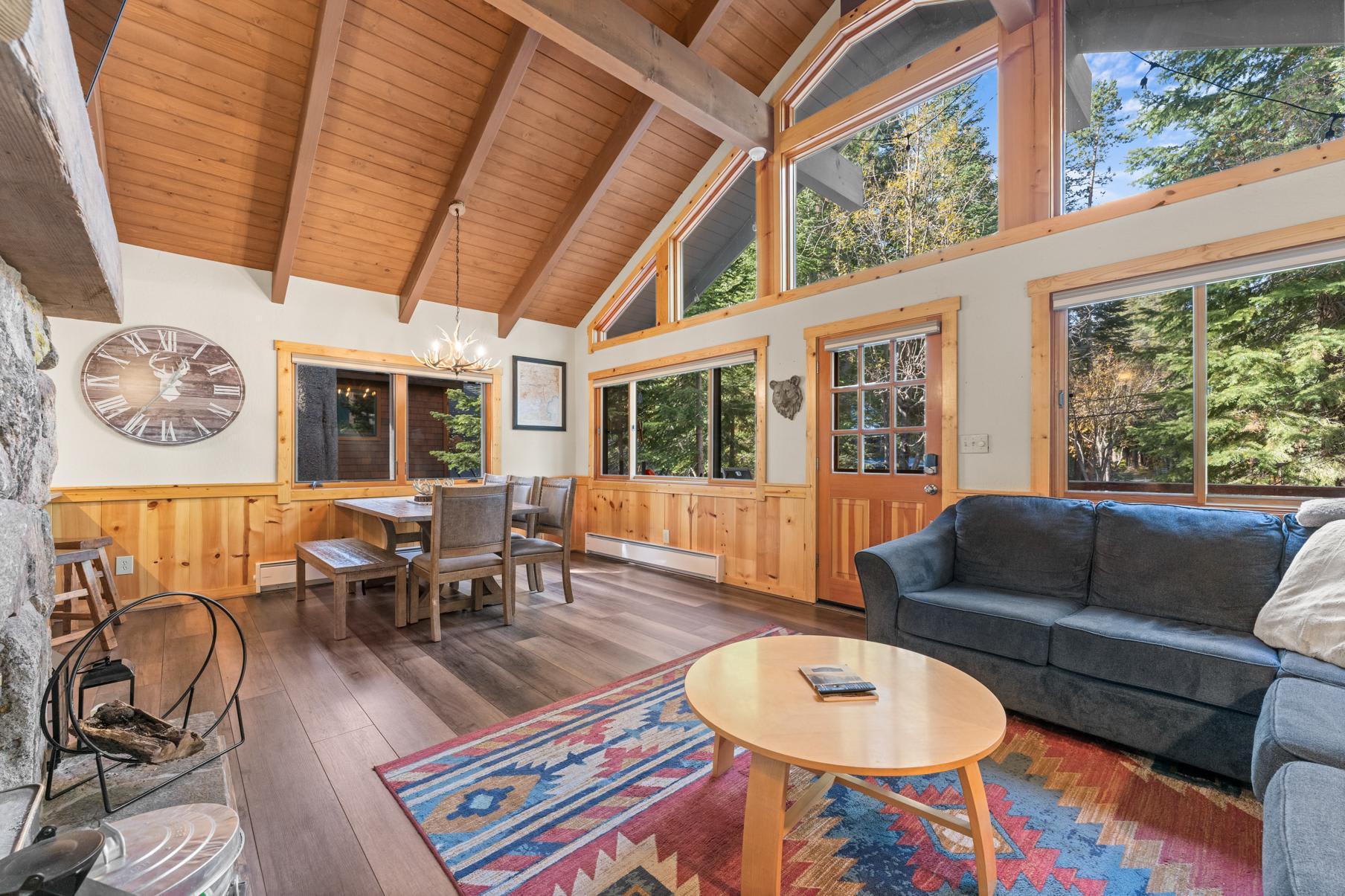 Cozy interior of a Truckee vacation rental with wood beams, large windows, and a colorful rug in the living area.