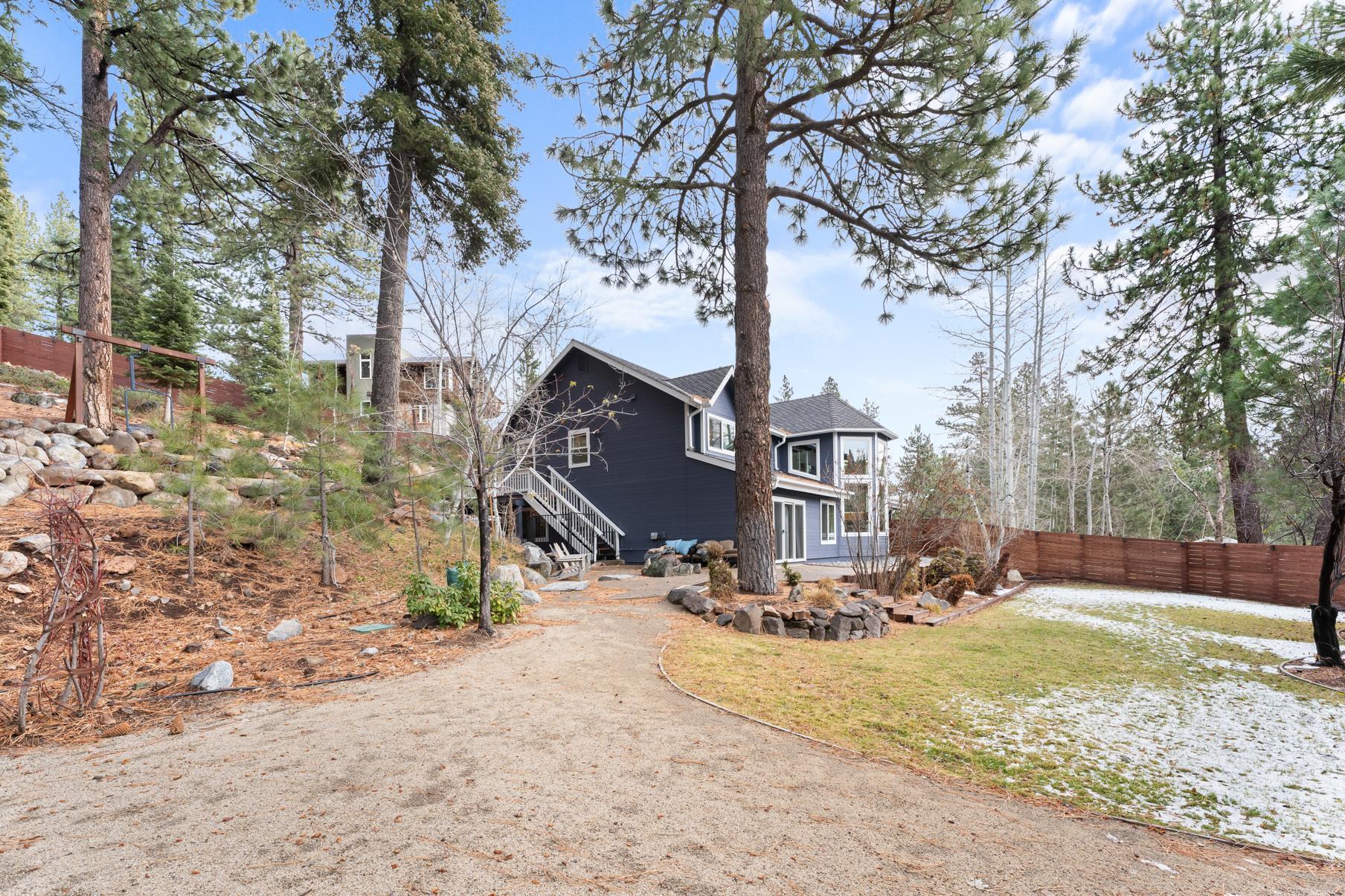 A cozy cabin-style vacation rental in Truckee surrounded by tall pine trees and a spacious yard with light snow.