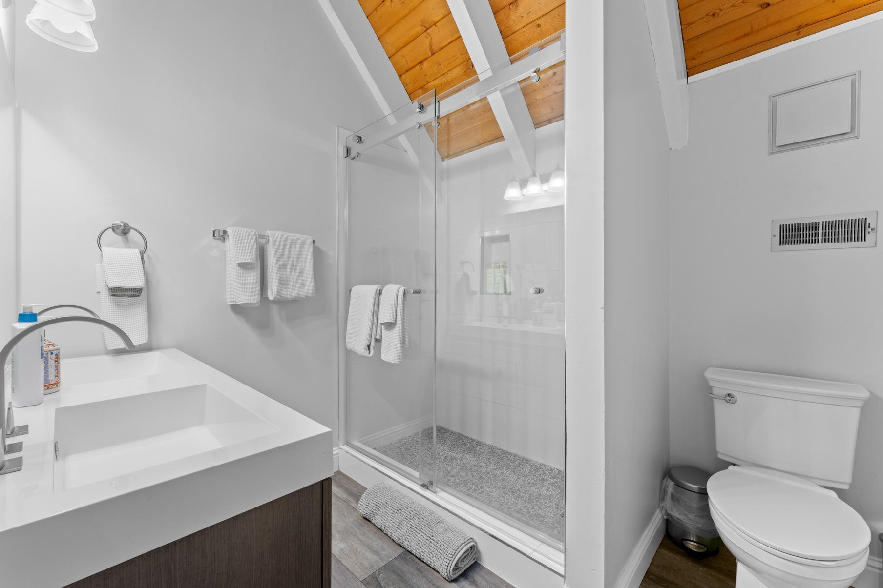 Modern bathroom in a Tahoe Vista vacation rental with glass shower, white sink, and wooden ceiling accents.