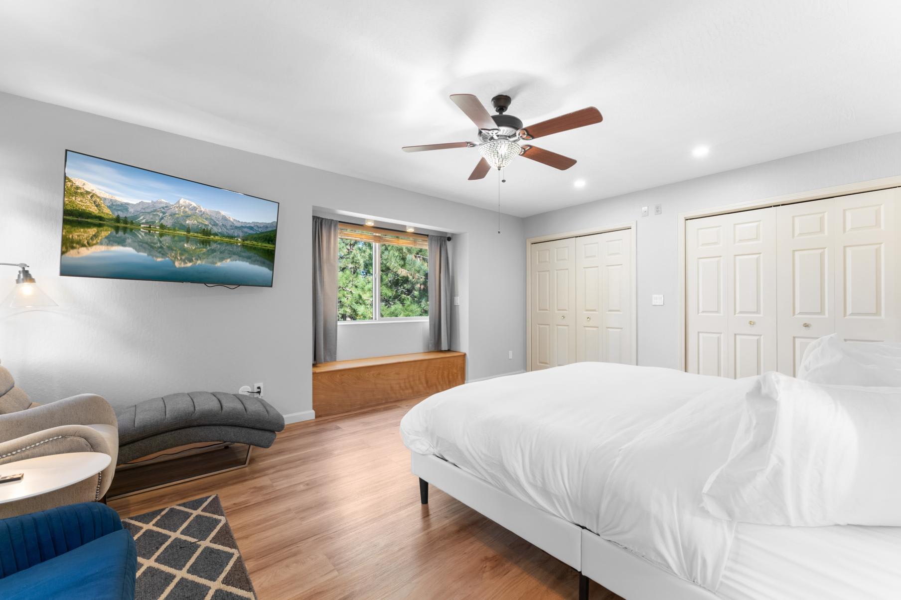 Modern bedroom in a Truckee vacation rental, featuring a cozy bed, chaise lounge, and a wall-mounted TV with scenic views.