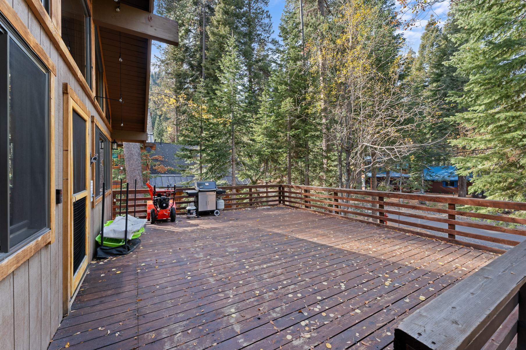 Spacious wooden deck at a vacation rental in Truckee, surrounded by trees, featuring a grill and snowblower.