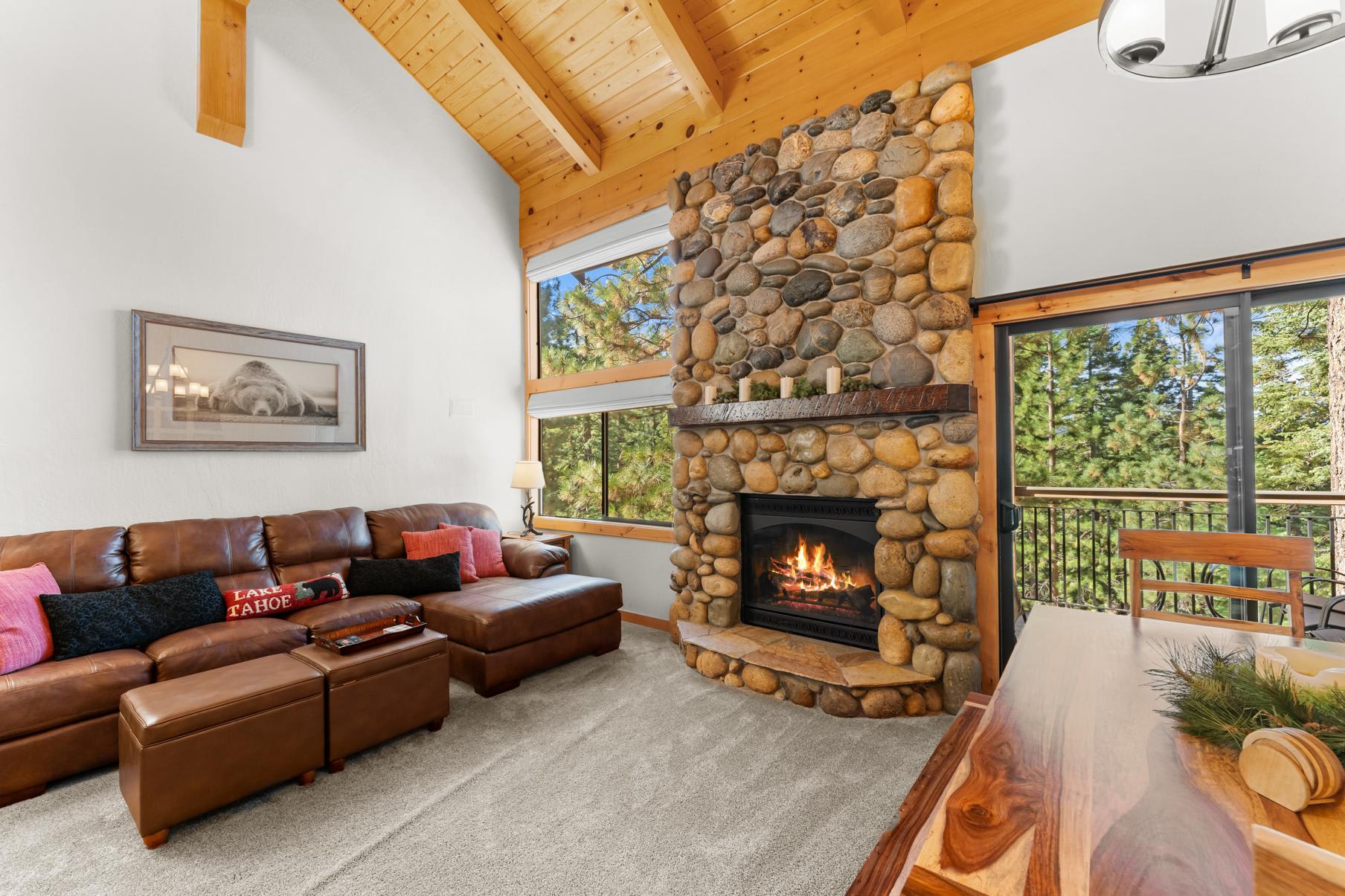 Cozy living room in a Truckee vacation rental with stone fireplace, leather couch, and large windows showcasing forest views.