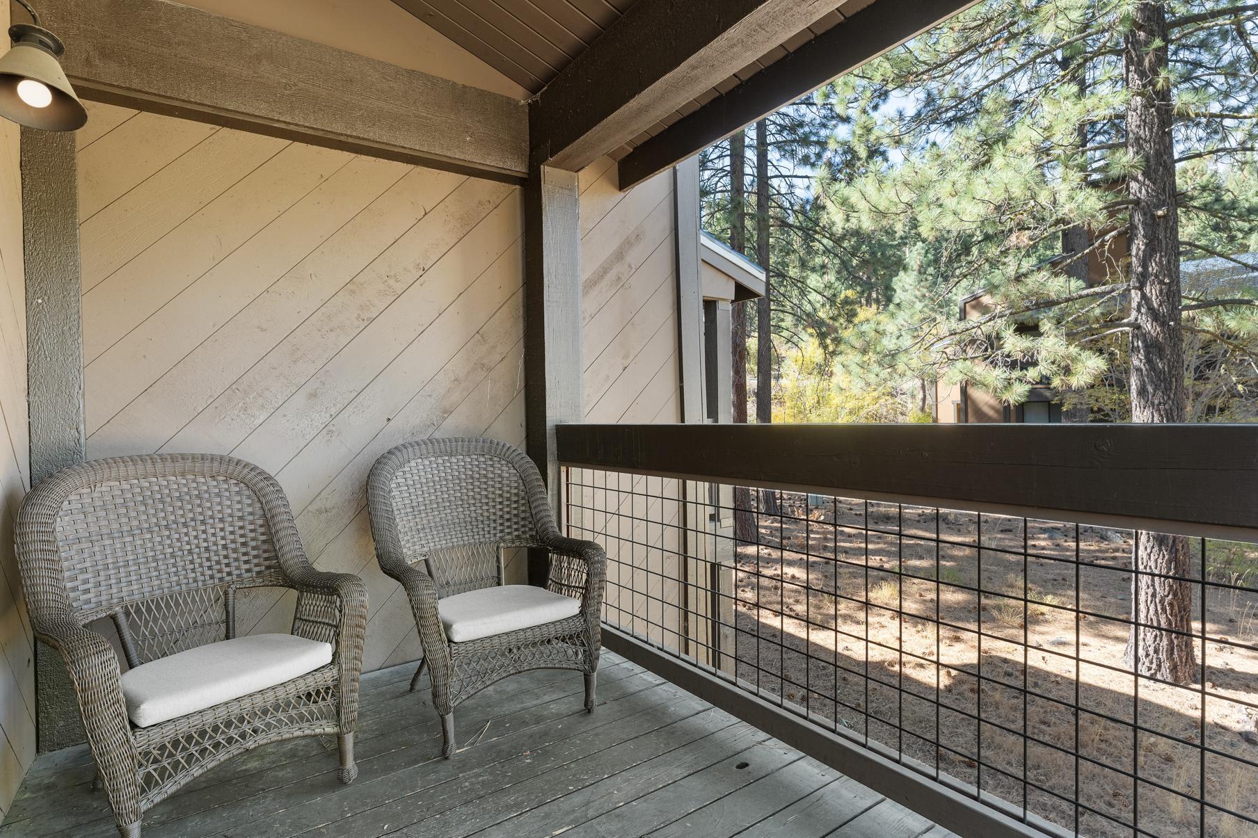 Vacation rental balcony in Truckee with two wicker chairs, surrounded by trees.