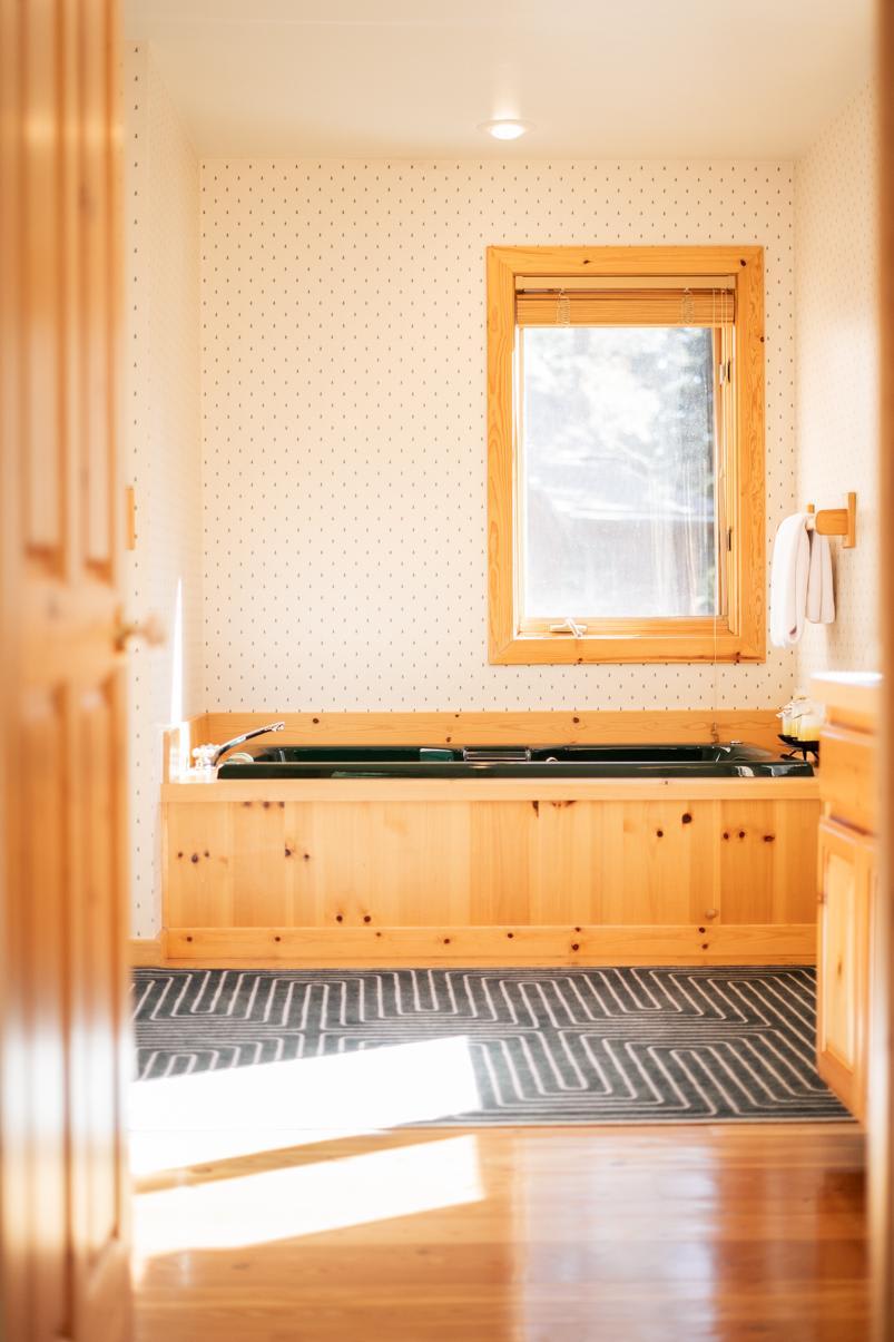 Cozy bathroom in a Truckee vacation rental with wood accents, sunlight streaming through a window, and a bathtub.