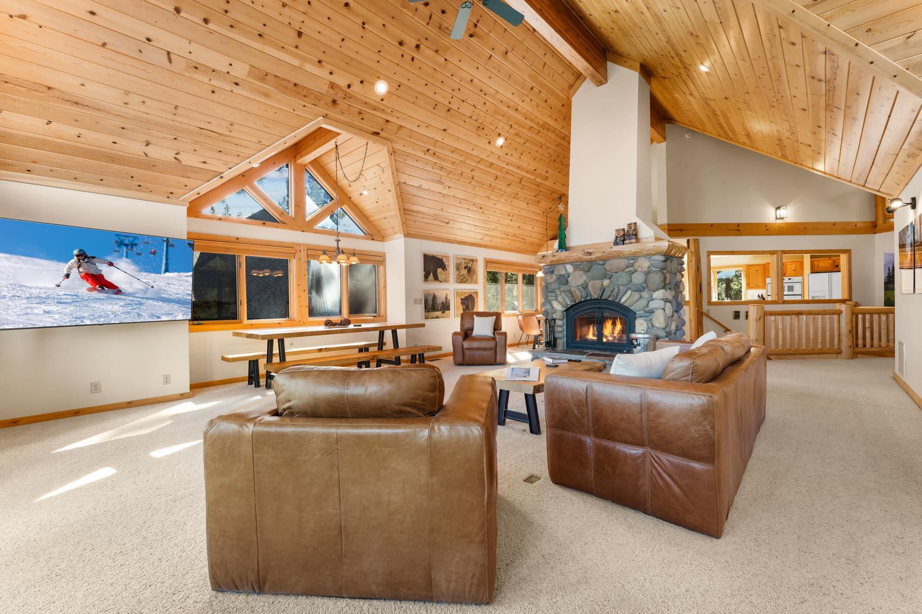 Spacious Truckee vacation rental with wooden interiors, cozy stone fireplace, and leather seating in a bright living area.