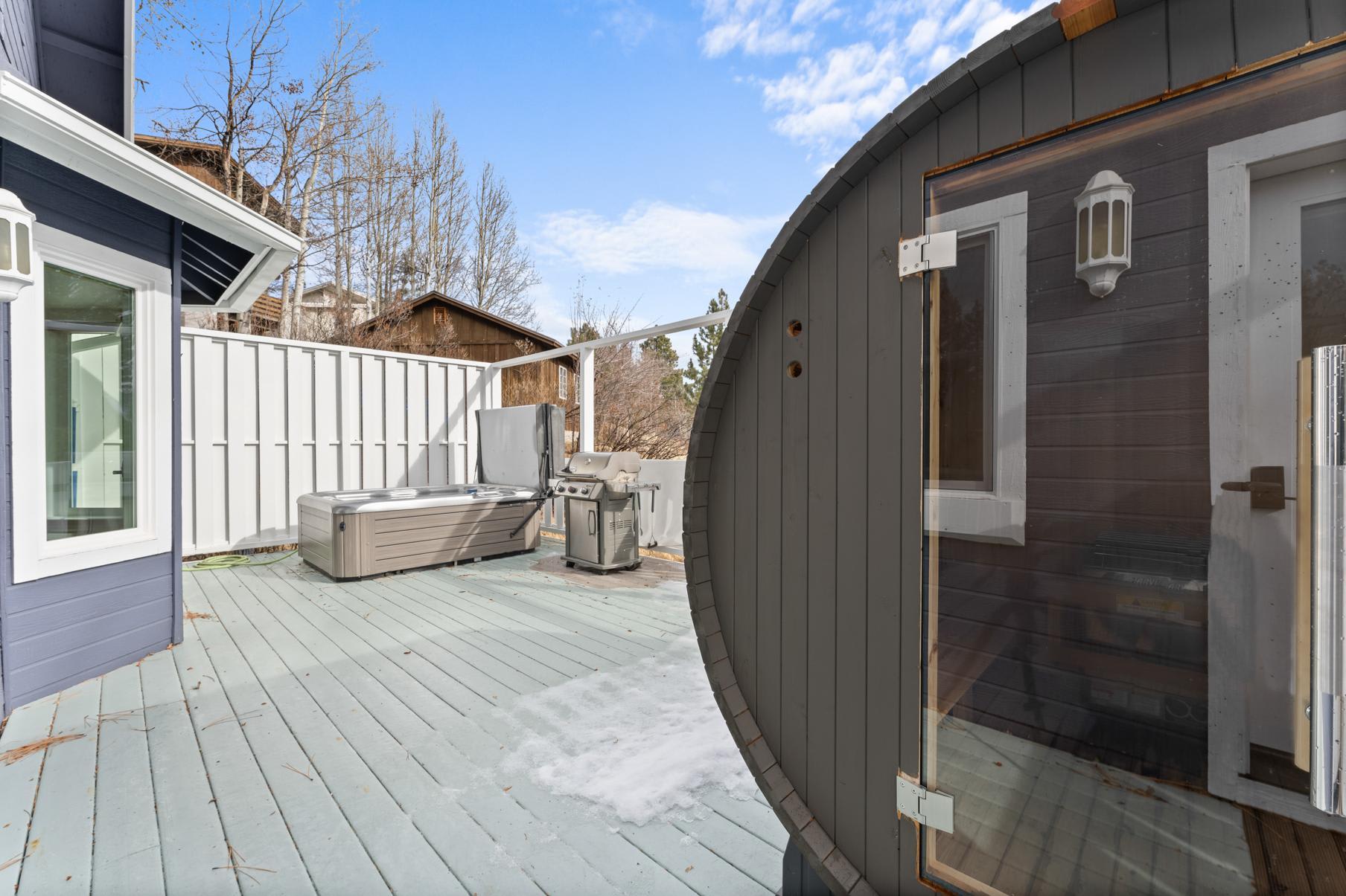 Truckee vacation rental with a spacious deck featuring a hot tub, barbecue grill, and barrel sauna surrounded by trees.