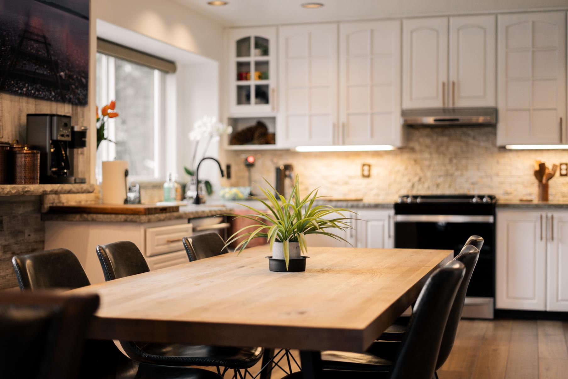 Modern kitchen in a Truckee vacation rental with wooden table, plant centerpiece, white cabinets, and sleek appliances.