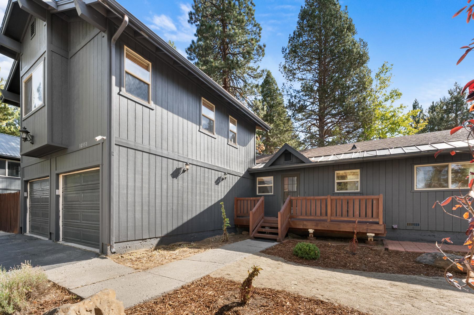 Gray vacation rental home in Truckee with wooden deck, surrounded by trees under a clear blue sky.