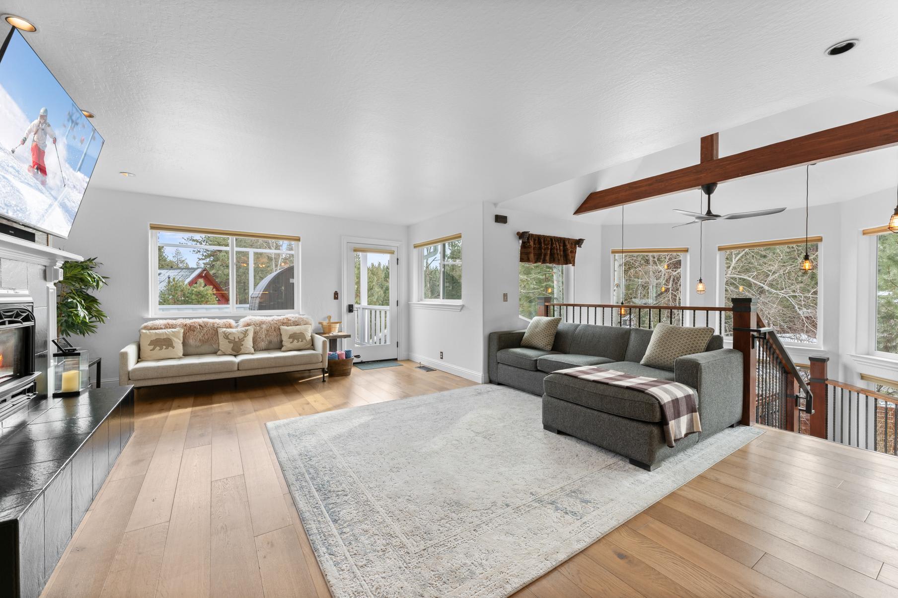 Bright living room in Truckee vacation rental with large windows, cozy sofas, and a TV showing a snowy scene.