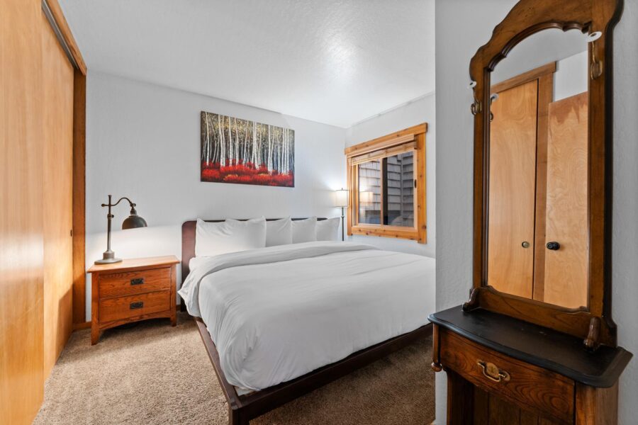 Cozy bedroom in Truckee vacation rental, featuring a large bed, rustic furniture, and a forest-themed painting on the wall.