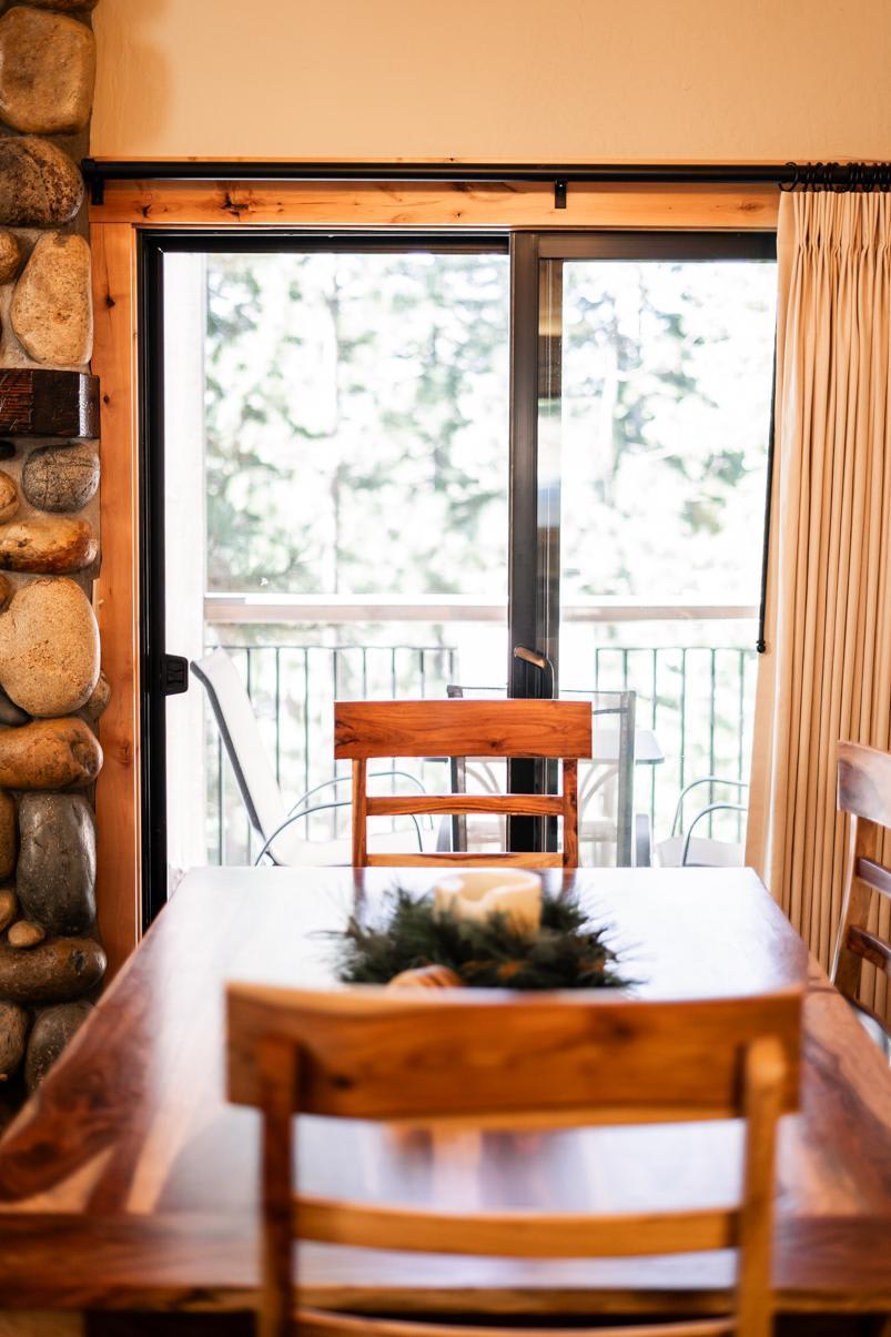 Cozy dining area in a Truckee vacation rental with wooden table and chairs, stone wall, and view of trees through glass doors.