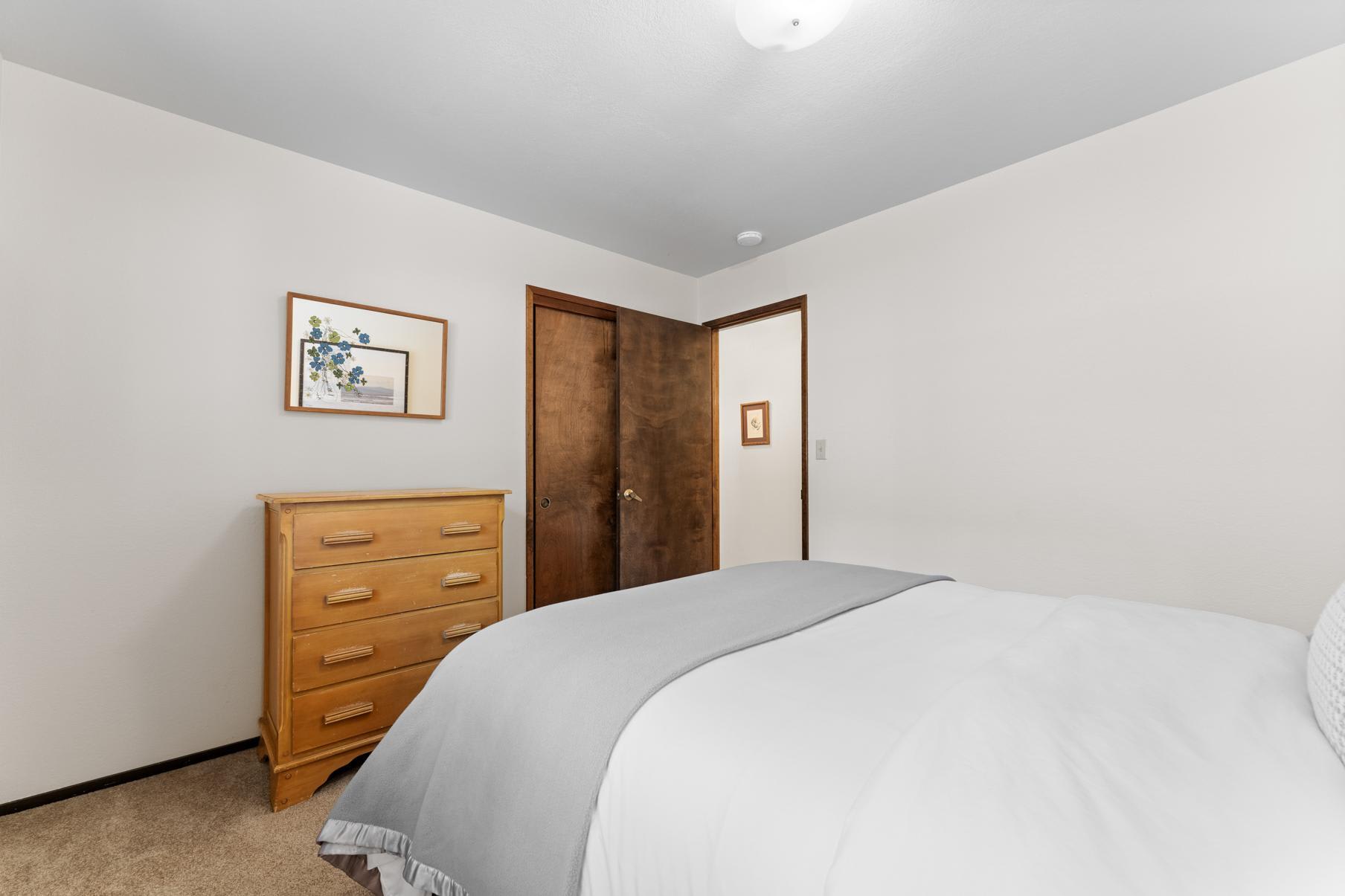 Bedroom in a Truckee vacation rental with a wooden dresser, art on the wall, and a neatly made bed with a gray blanket.