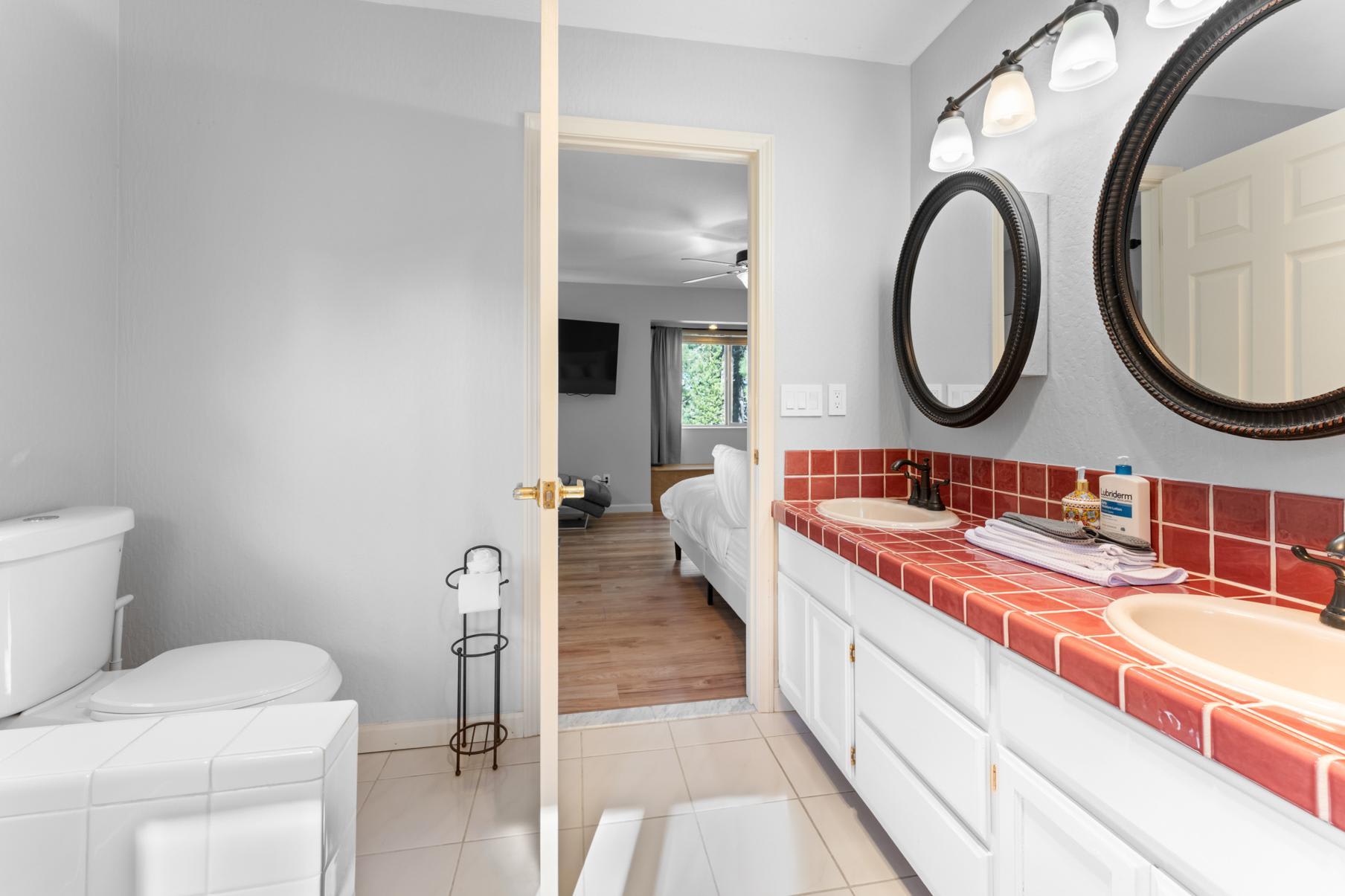 Bathroom with red-tiled double sinks in a Truckee vacation rental. Bedroom visible through an open door.