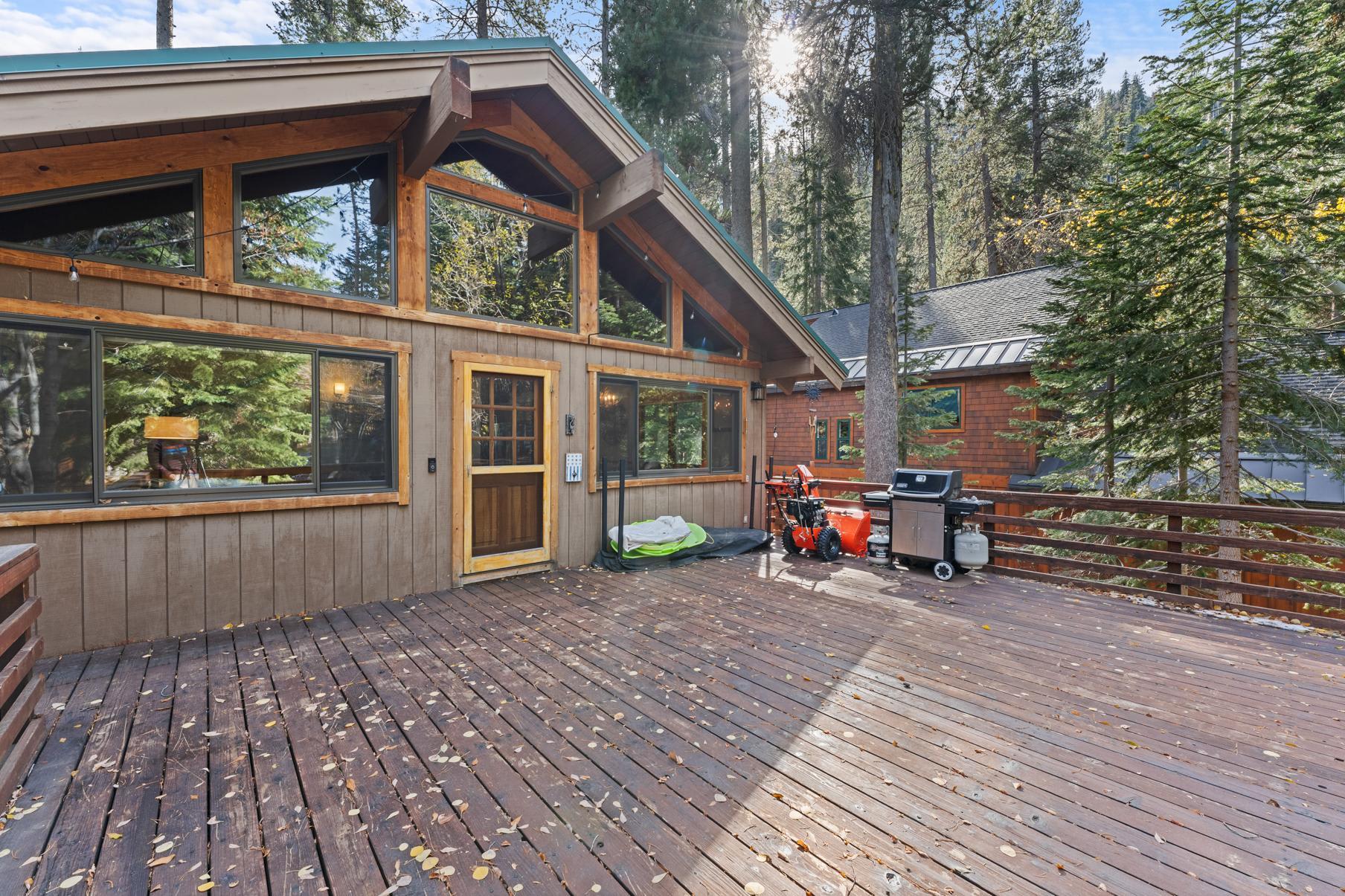 Wooden deck of a Truckee vacation rental, surrounded by trees, features a grill and large sliding windows.