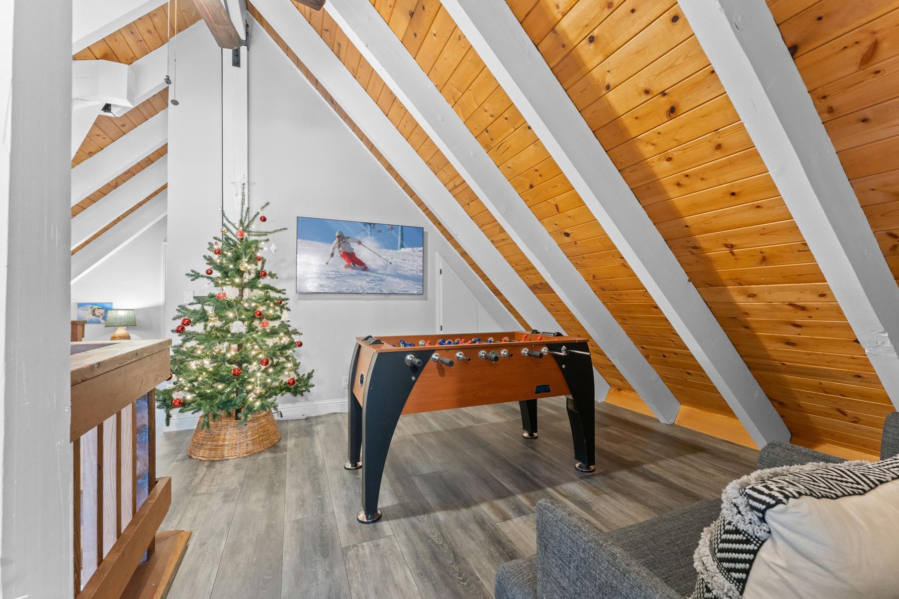 Cozy Tahoe Vista vacation rental loft with a foosball table, decorated Christmas tree, and sloped wooden ceiling.