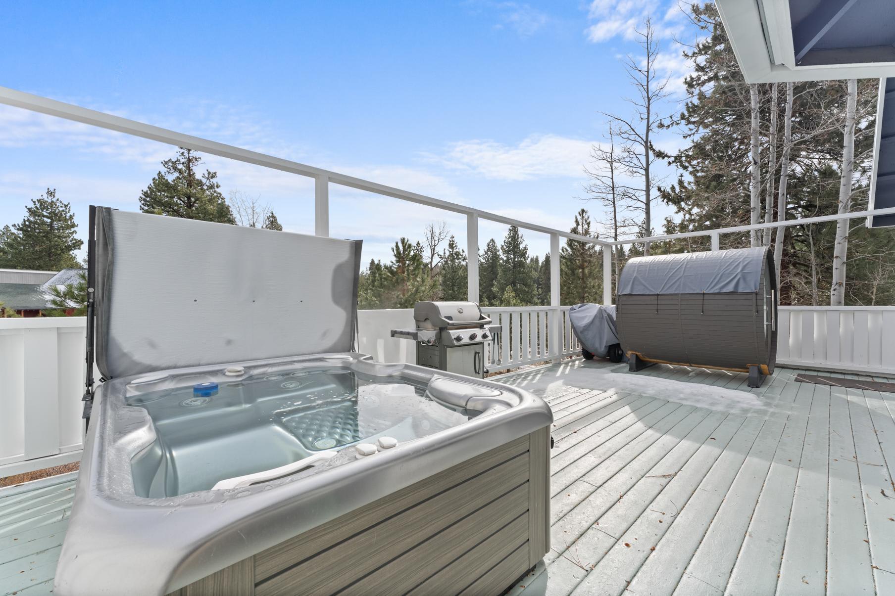 Deck in Truckee vacation rental with hot tub, grill, and trees in the background under a clear blue sky.