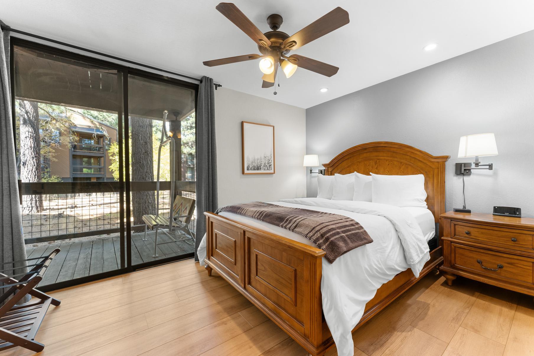 Cozy bedroom in a Truckee vacation rental with a wooden bed, bedside tables, and a balcony view of trees.