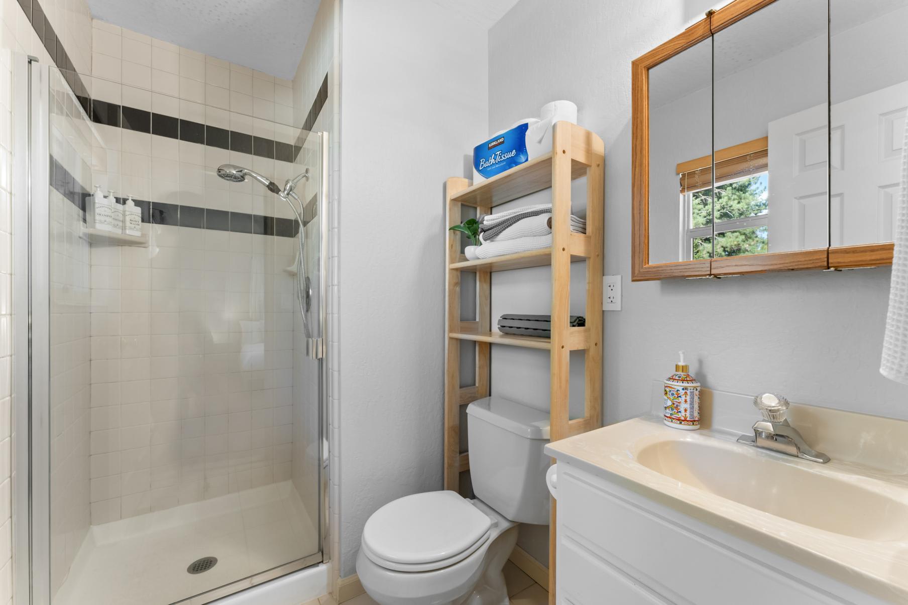 Small bathroom in a Truckee vacation rental with a shower, toilet, and shelving stocked with towels and toiletries.