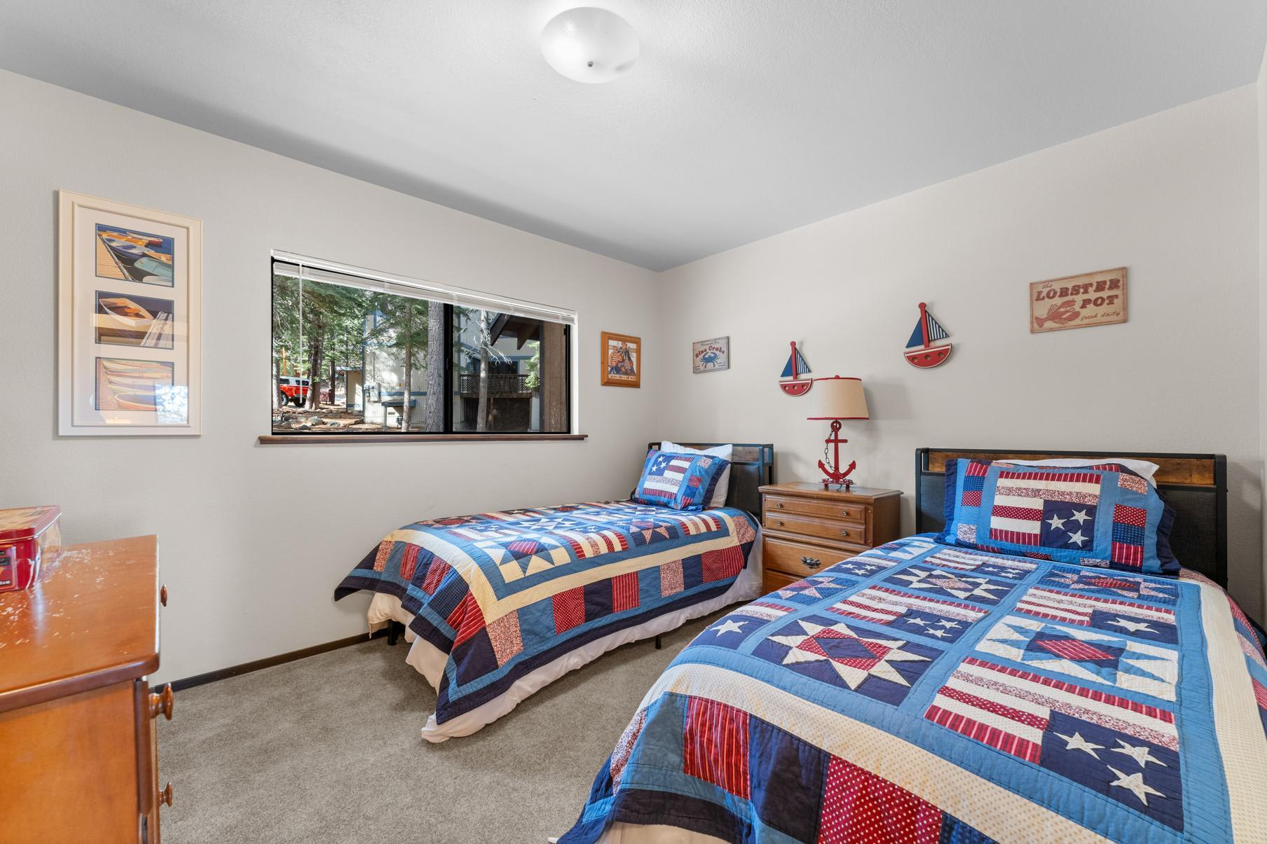 Cozy twin bedroom in a Truckee vacation rental, featuring nautical-themed quilts and decor with a forest view.