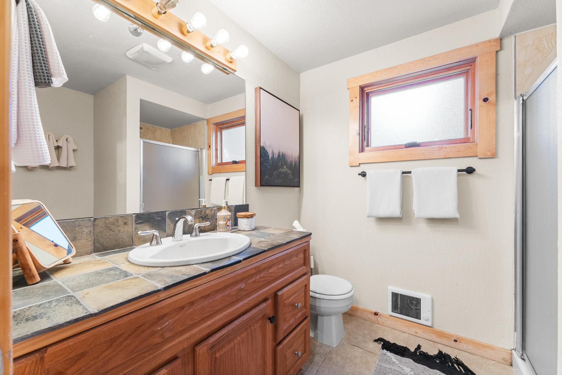 Bathroom in a Truckee vacation rental with tiled sink, wooden cabinets, and a shower, featuring a window and modern decor.