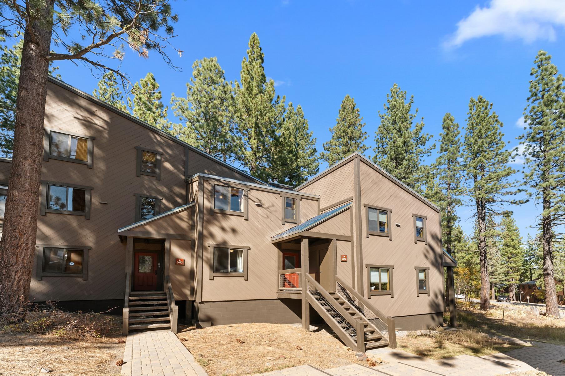 Brown vacation rental home in Truckee, surrounded by tall pine trees under a clear blue sky.