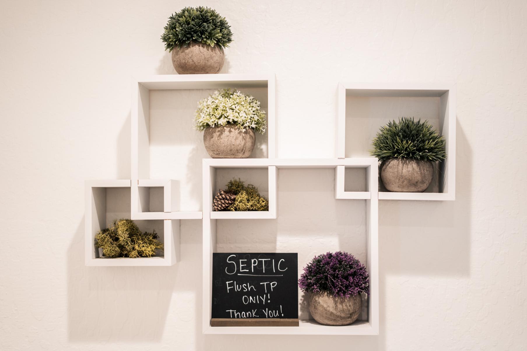 Decorative wall shelves with plants and a sign in a Truckee vacation rental bathroom.