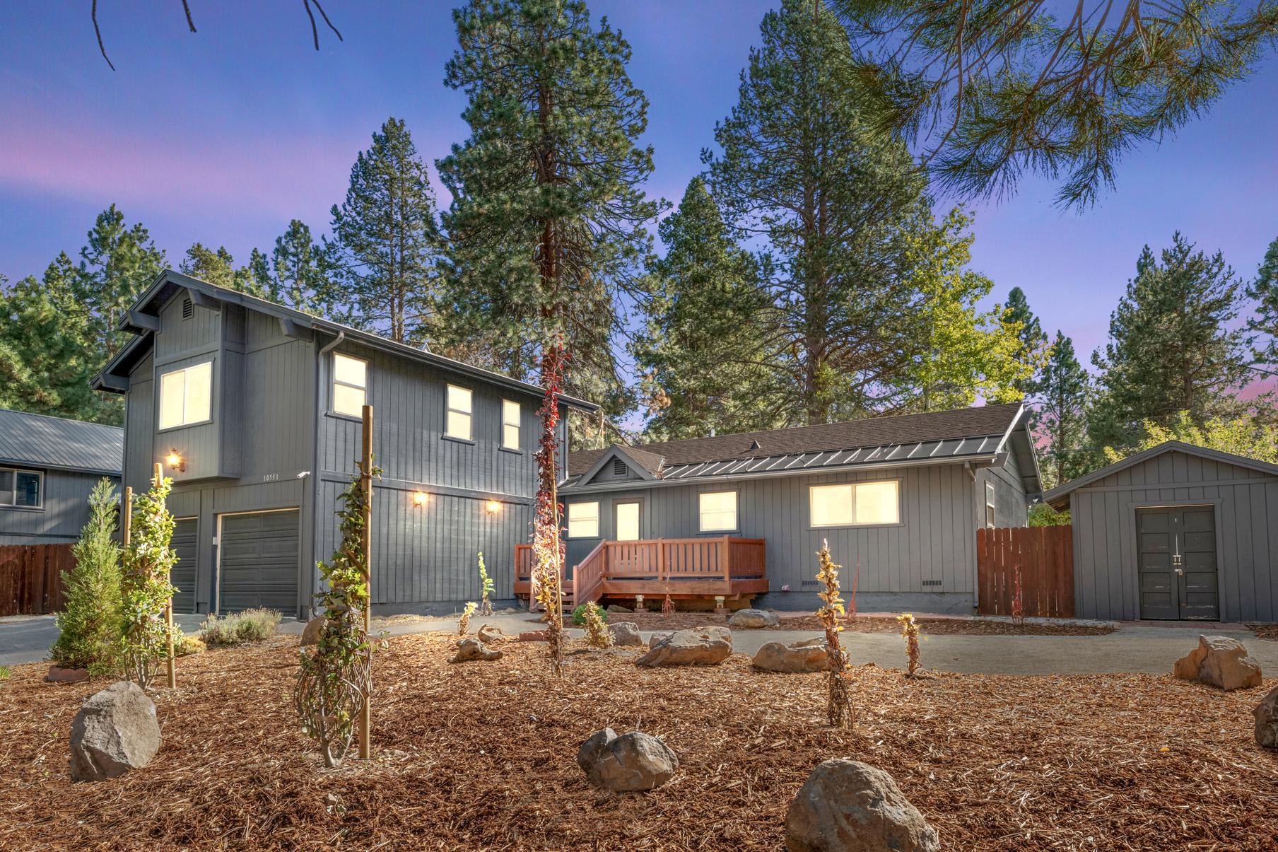 Modern gray vacation rental house in Truckee, surrounded by tall trees and a landscaped yard at dusk.