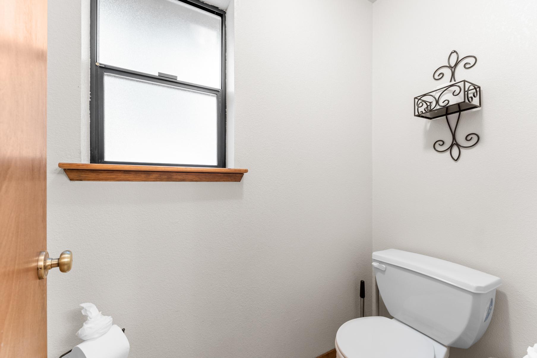 Bathroom view in a Truckee vacation rental with a white toilet, decorative shelf, and frosted window.