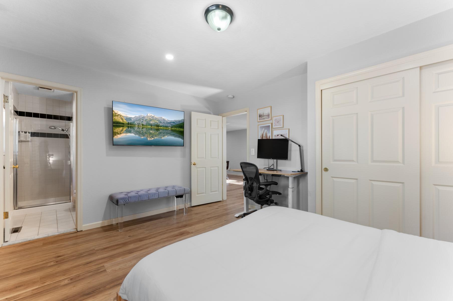 Modern bedroom in Truckee vacation rental with wooden floors, TV, desk, and en-suite bathroom.