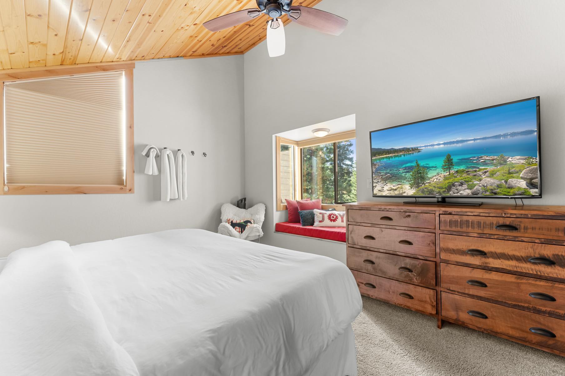 Cozy bedroom in Truckee vacation rental with a TV, wooden dresser, and a window seat offering a forest view.