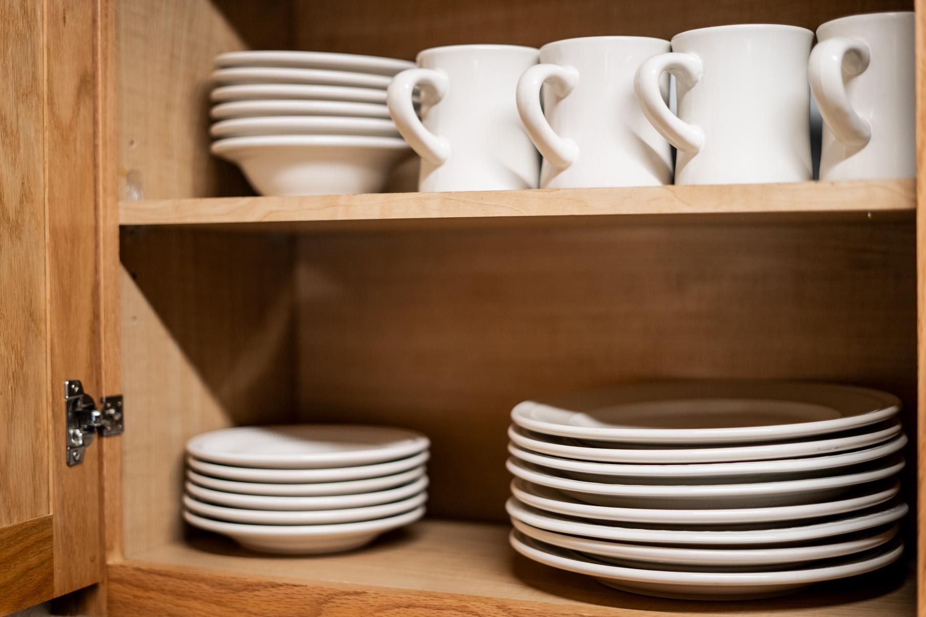 White dishes and mugs neatly arranged in a wooden cabinet of a Truckee vacation rental kitchen.